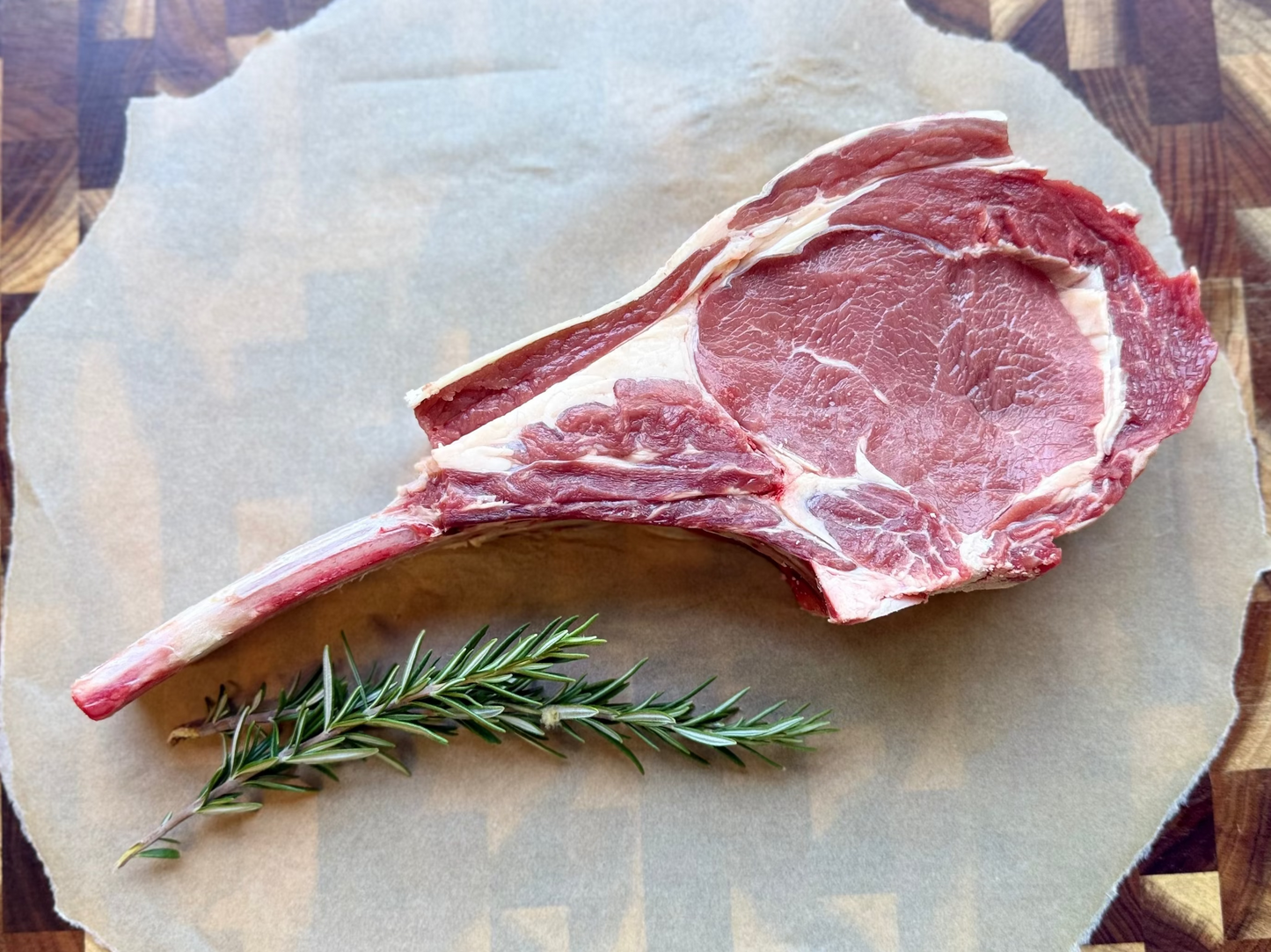 Tomahawk with a sprig of rosemary on a piece of paper on a wooden cutting board.