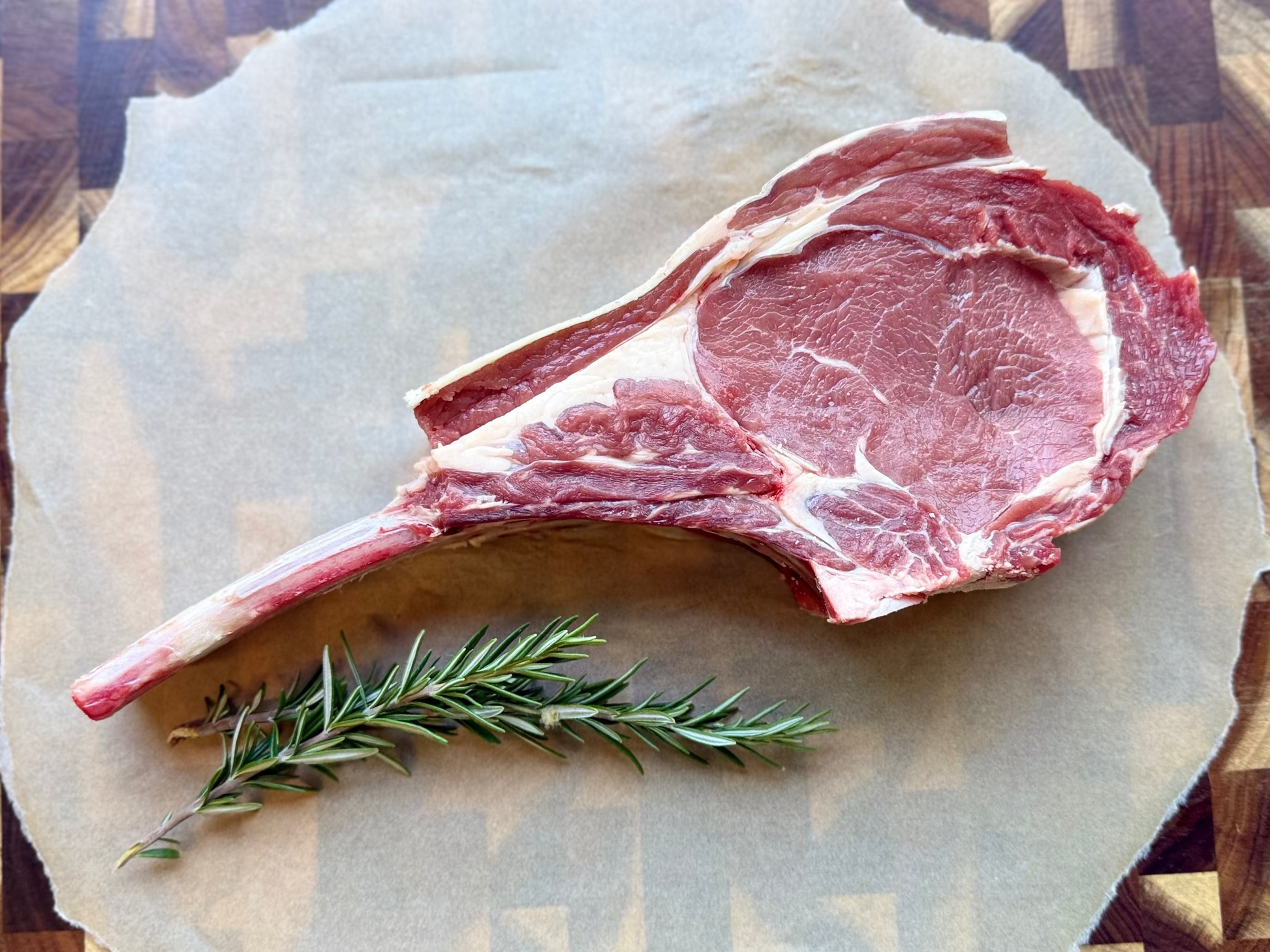 Tomahawk with a sprig of rosemary on a piece of paper on a wooden cutting board.